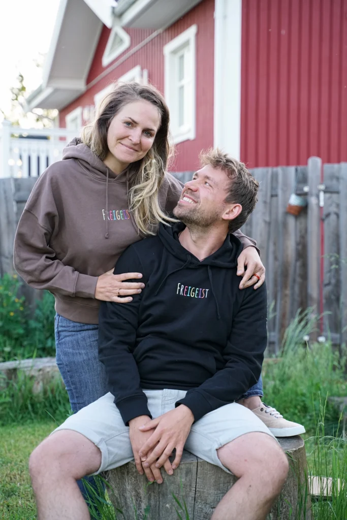 Max und Noreen lachen Zuhause draußen im Freigeist Merch Hoodie und T-Shirt.