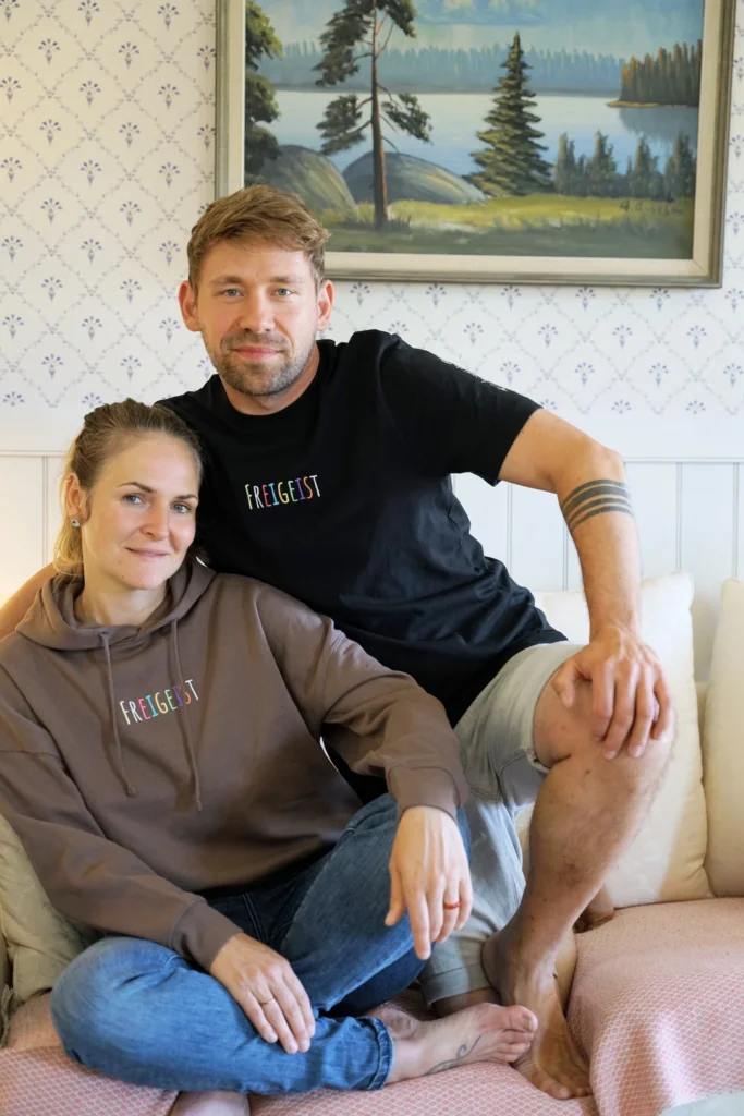 Max und Noreen lachen Zuhause im Freigeist Merch Hoodie und T-Shirt.